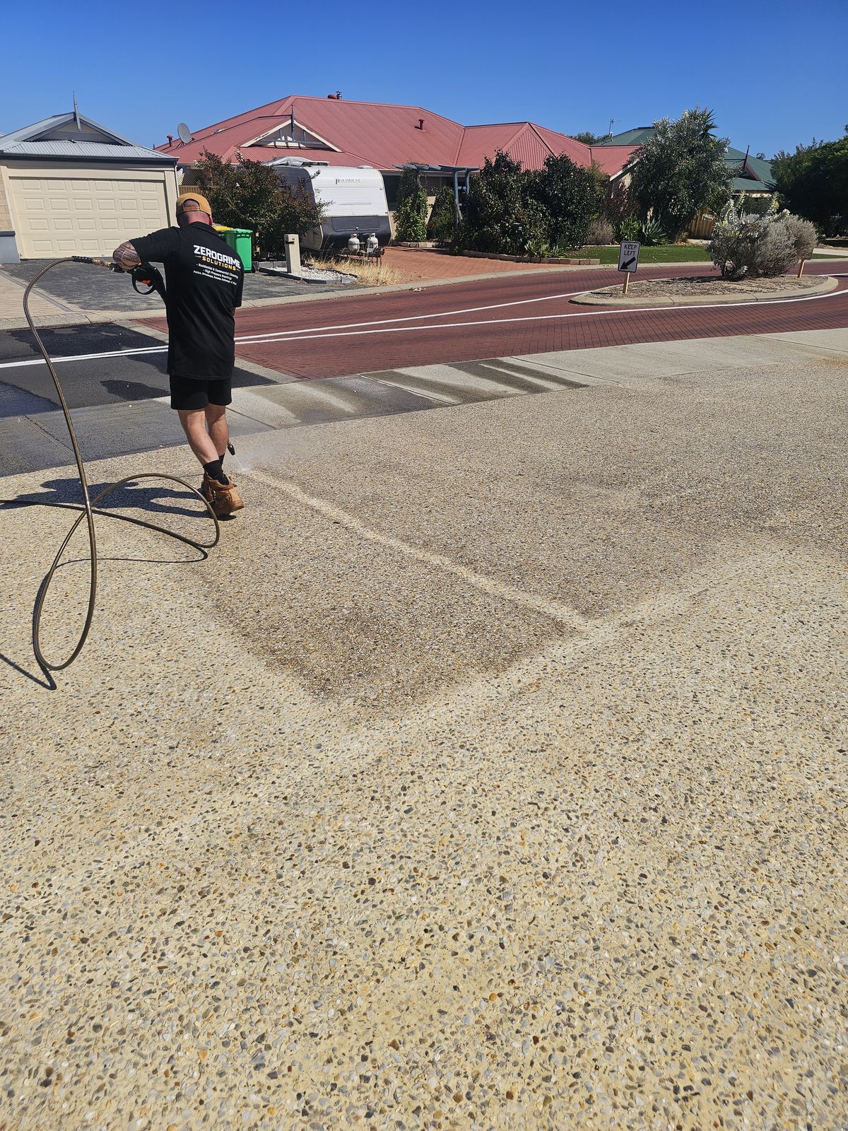ZeroGrime Solutions pressure cleaning an exposed aggregate driveway in Australind, showing the cleaned section next to the untreated concrete